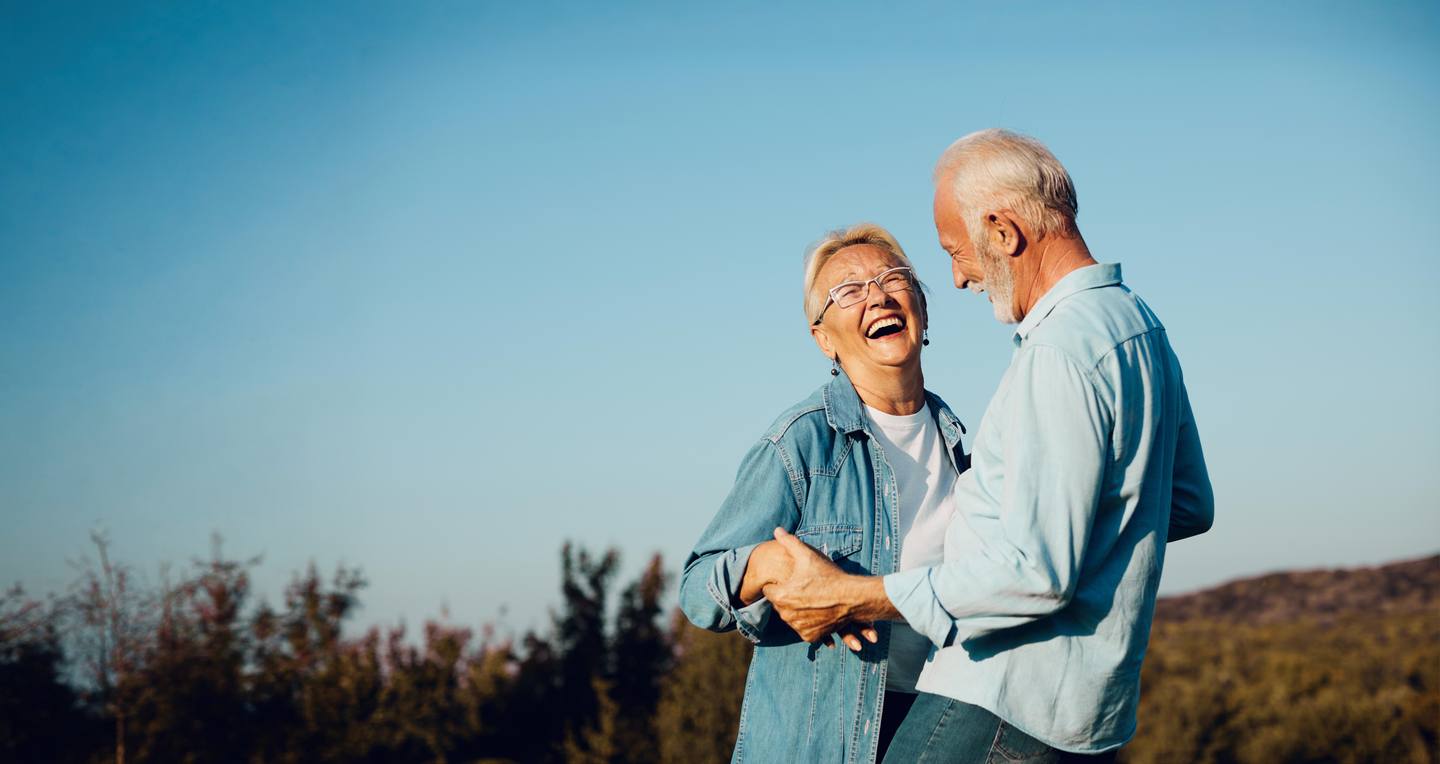 A smiling older couple dancing outdoors at sunset